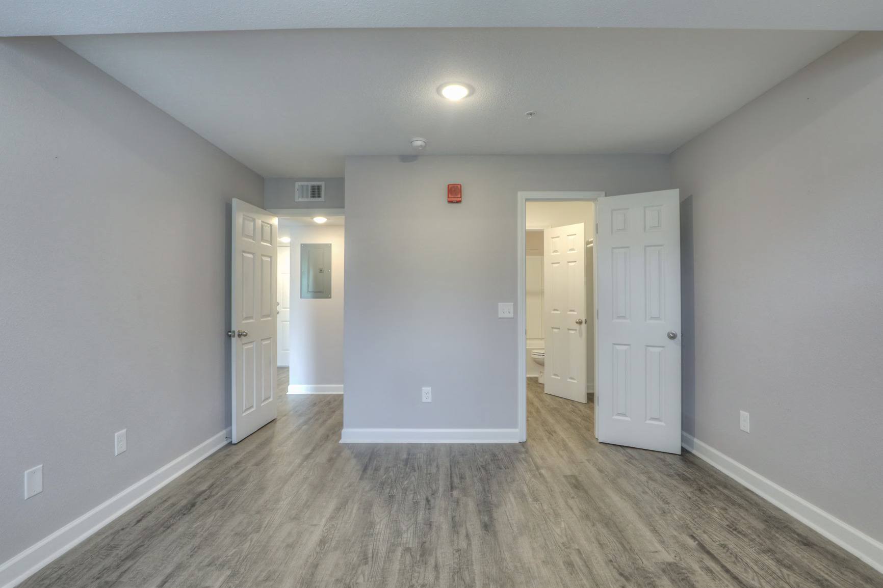 A room with white walls and wood flooring with two doors.